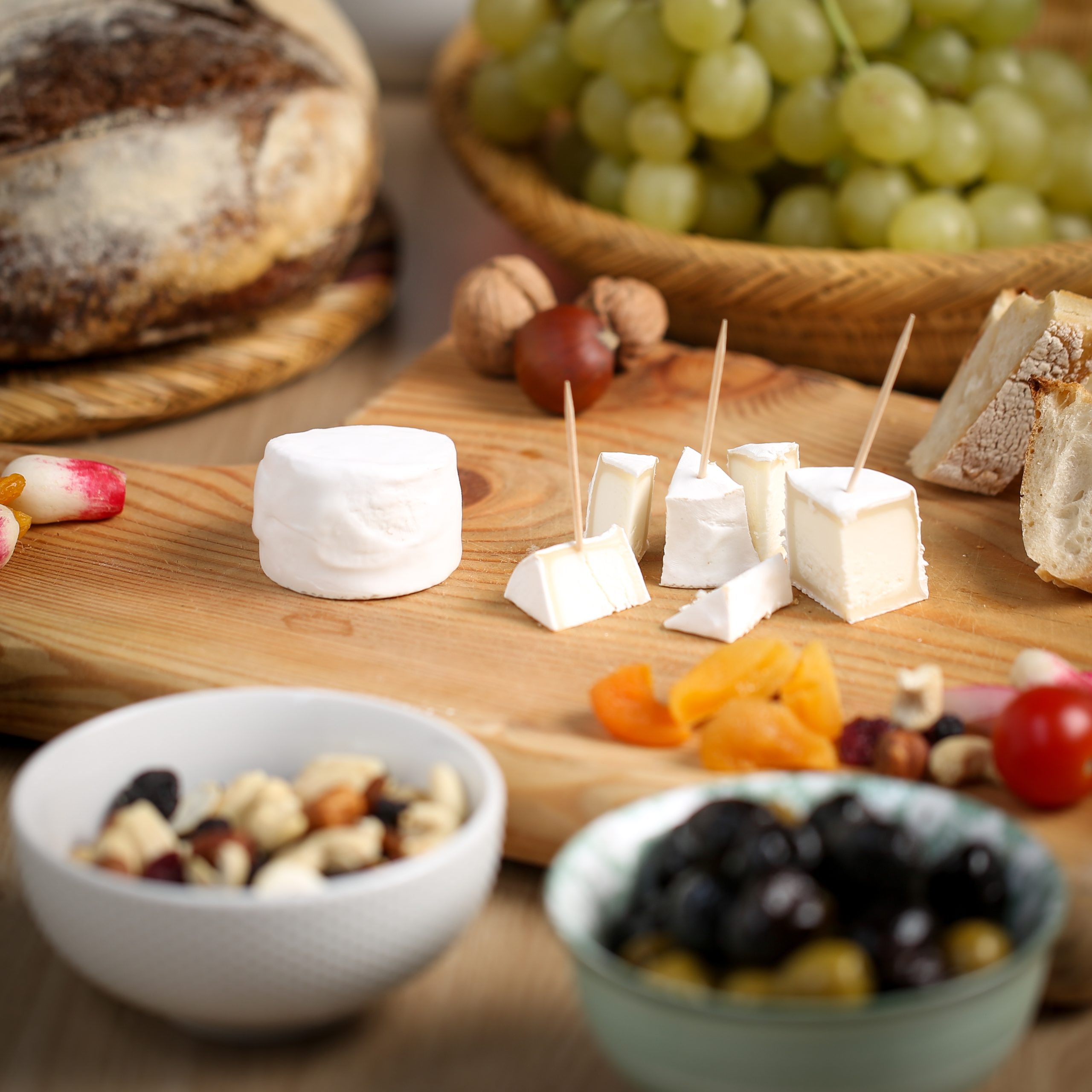 Plateau avec du pain, du raisin, des radis et deux petits fromages de chèvre “Les P’tit Ronds” entier et en morceaux pour piquer et partager en convivialité.